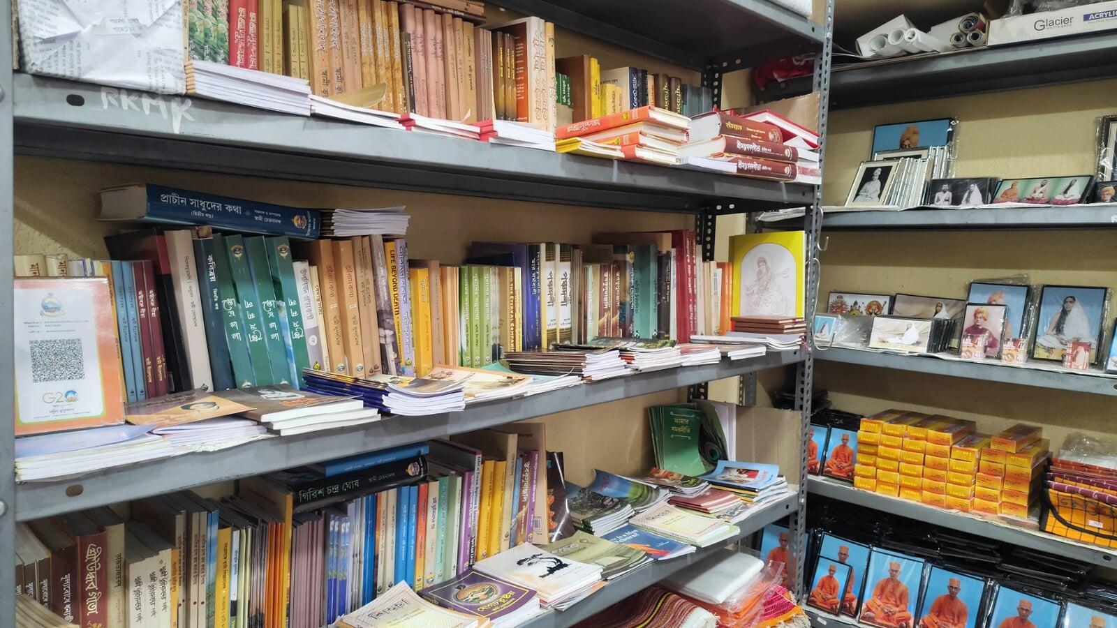 Interior view of a well-lit bookstore of Ramakrishna Math Madurai, with a large collection of books on white shelves and a staircase in the background